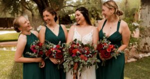 A bride poses with her bridesmaids wearing forest green dresses. 