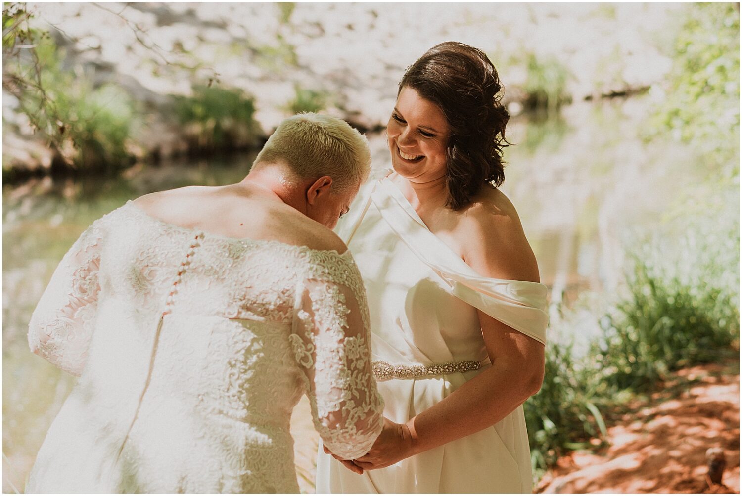 Two brides laugh beside a creek in Sedona.