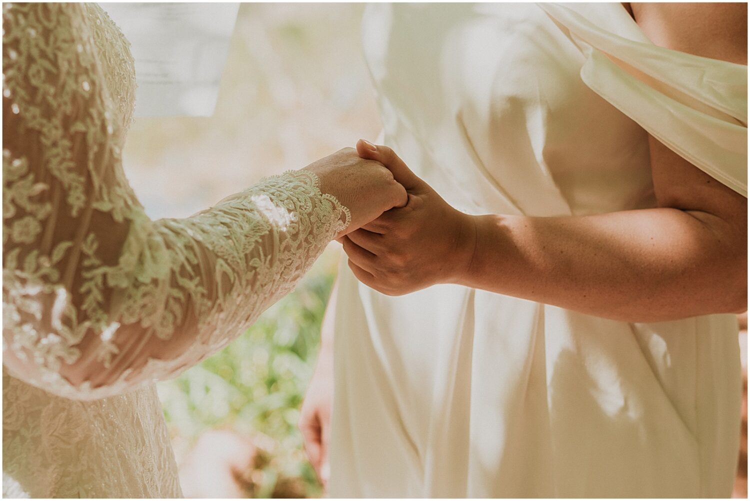 Two brides hold hands in the shade.
