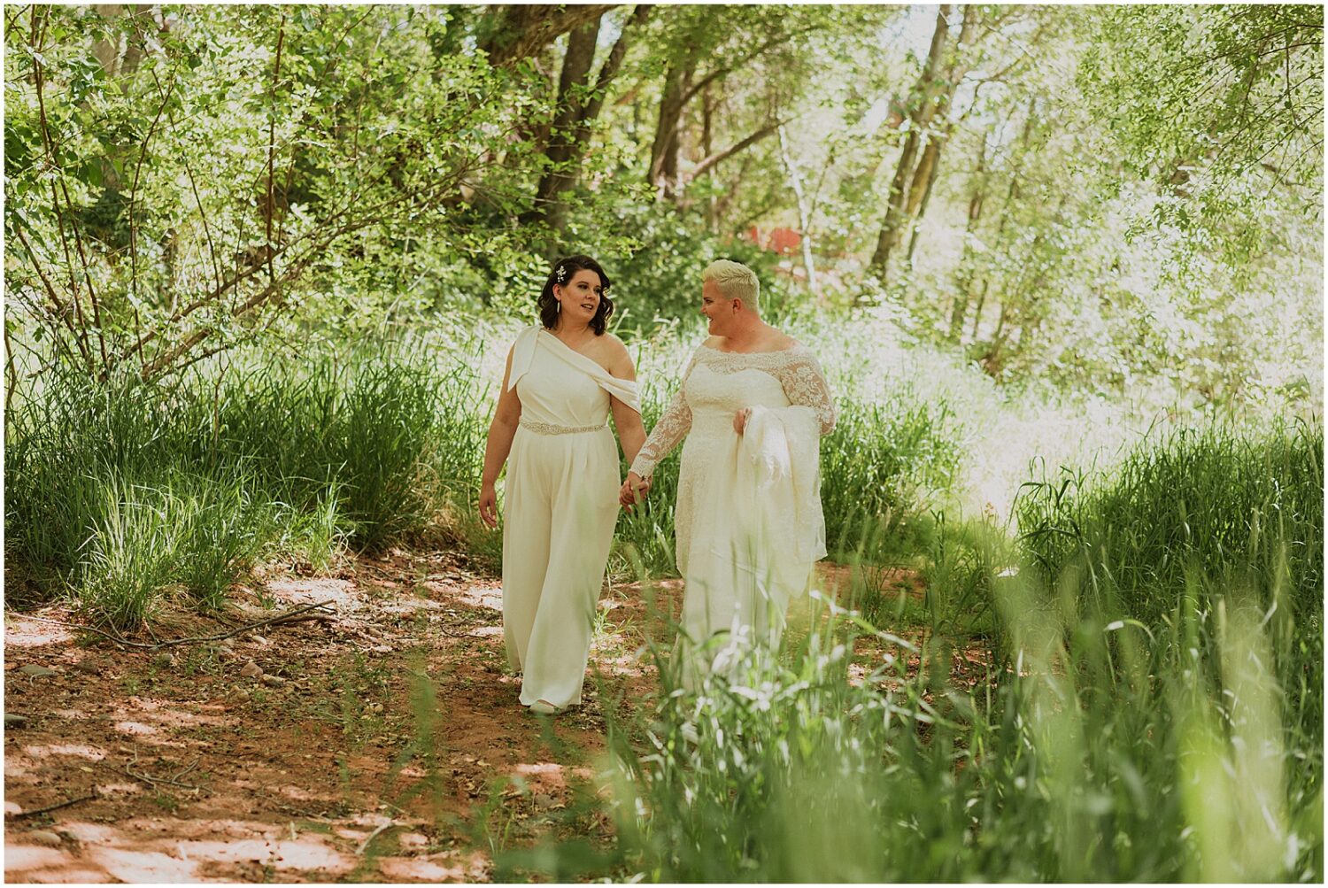 Two brides walk down a wooded path towards an Arizona wedding photographer.