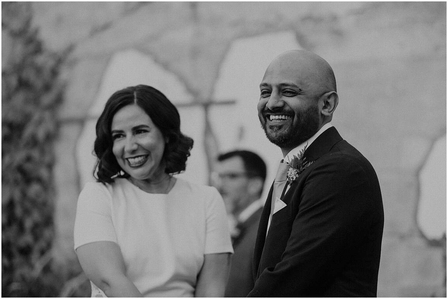 A bride and groom smile at their wedding guests.
