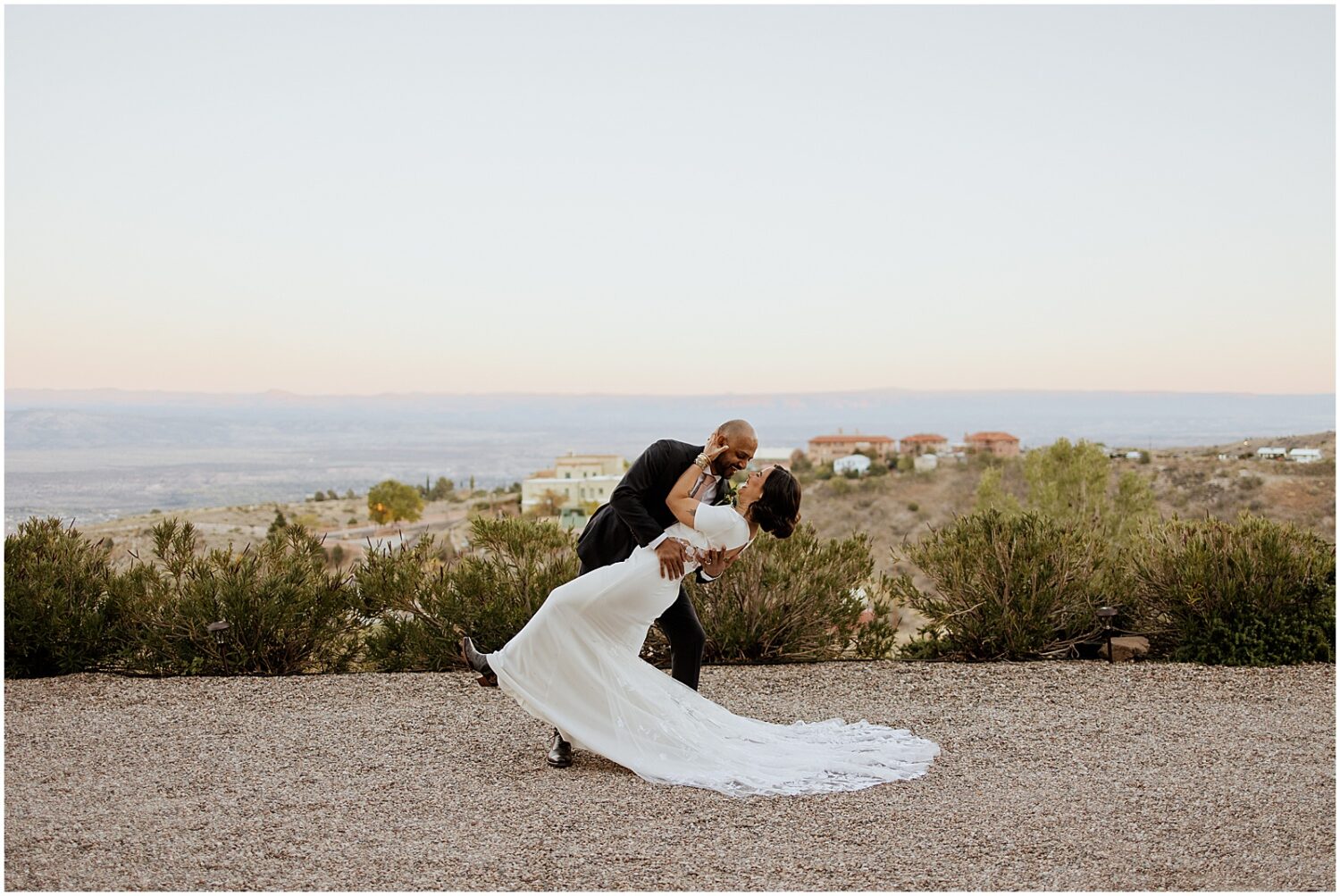A groom dips a bride for a kiss with Jerome in the background.