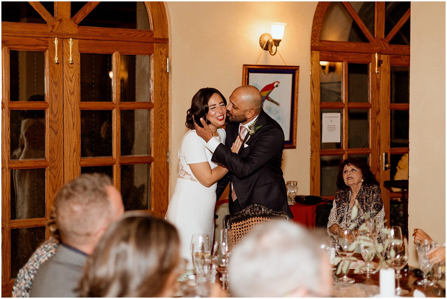 A groom kisses a bride's cheek at a reception.
