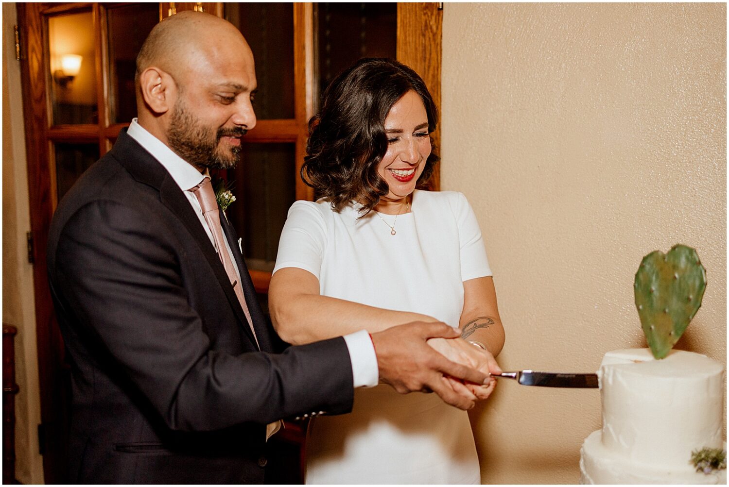 A bride and groom cut a tiered wedding cake decorated with cactus paddles.