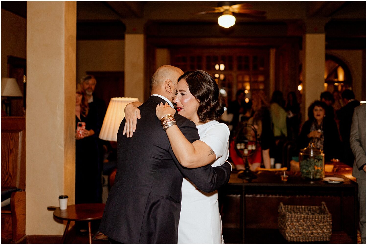 A bride and groom embrace at the edge of a wedding reception.