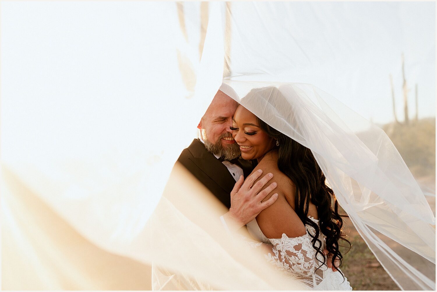 A bride and groom embrace as her veil floats around them.