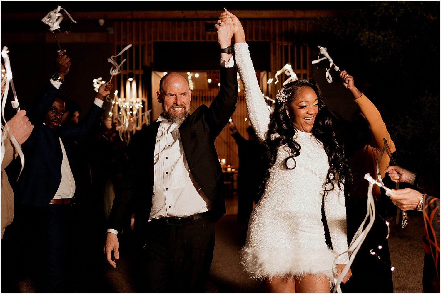 A bride and groom wave to guests at their wedding exit.