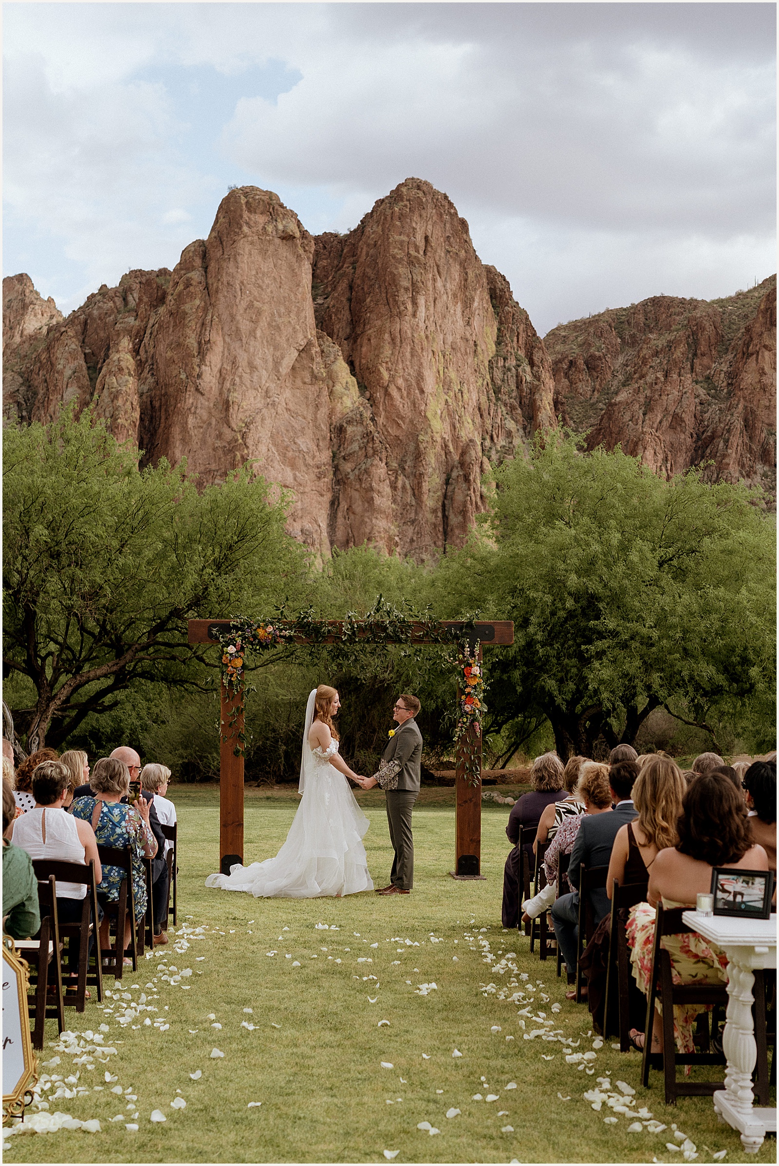Two marriers hold hands under an arch at a Saguaro Lake Ranch wedding ceremony.