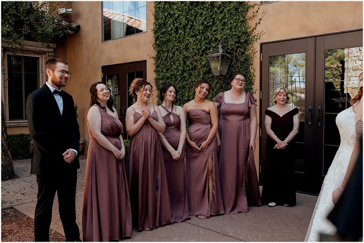 Bridesmaids smile as a bride walks out of a door for a first look with bridesmaids.