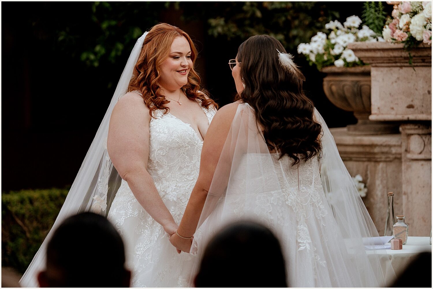 Two brides hold hands during a wedding ceremony.