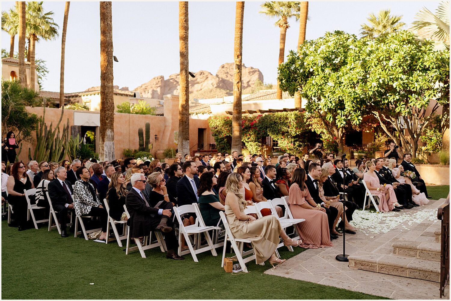 Wedding guests sit in chairs to watch a garden wedding ceremony.