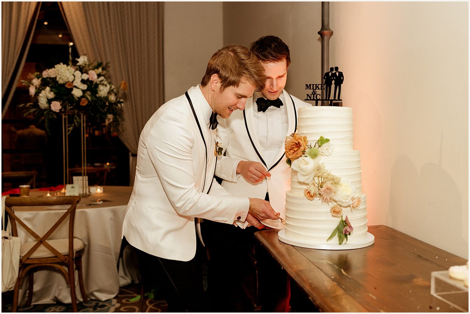 Two grooms cut a tiered wedding cake.