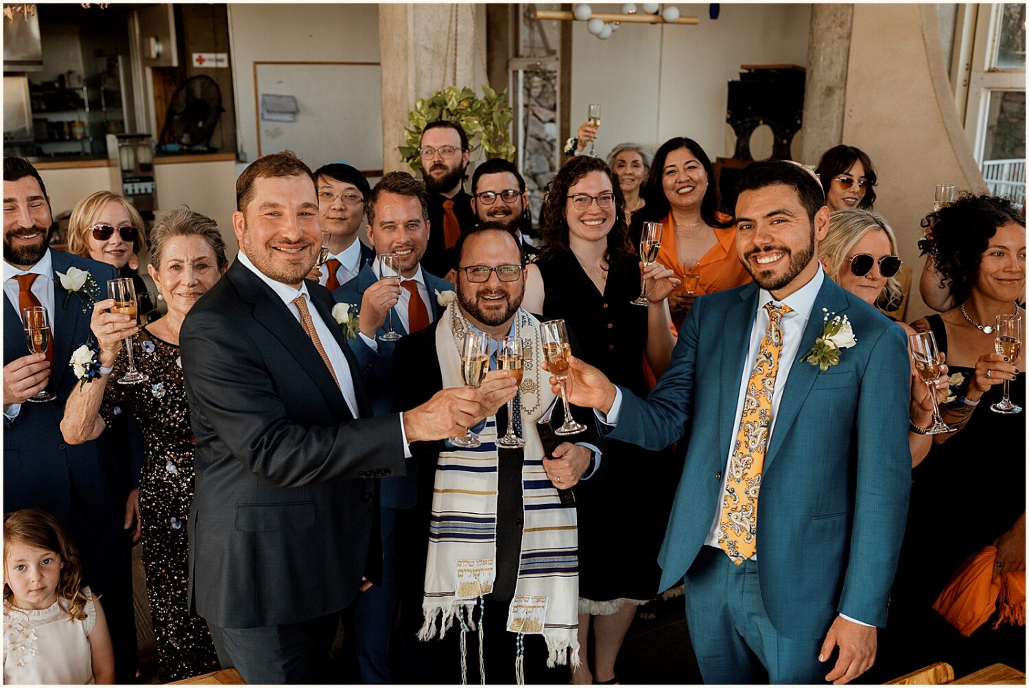 Grooms raise champagne glasses with their rabbi and family.