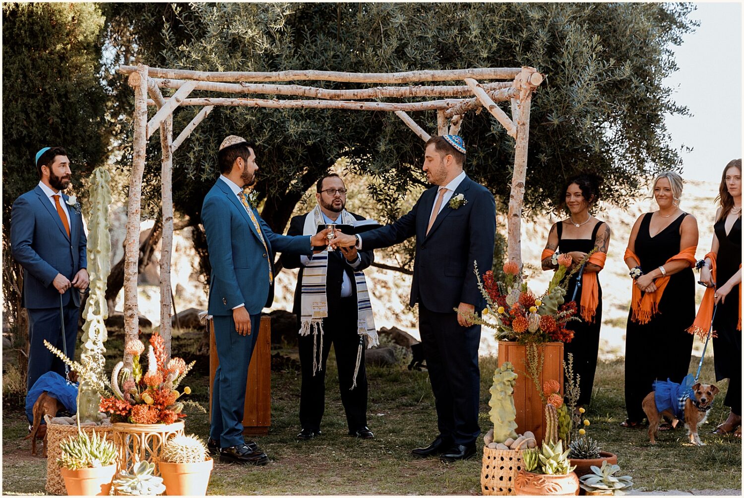 A groom passes a kiddush cup to his husband during a Jewish wedding ceremony.