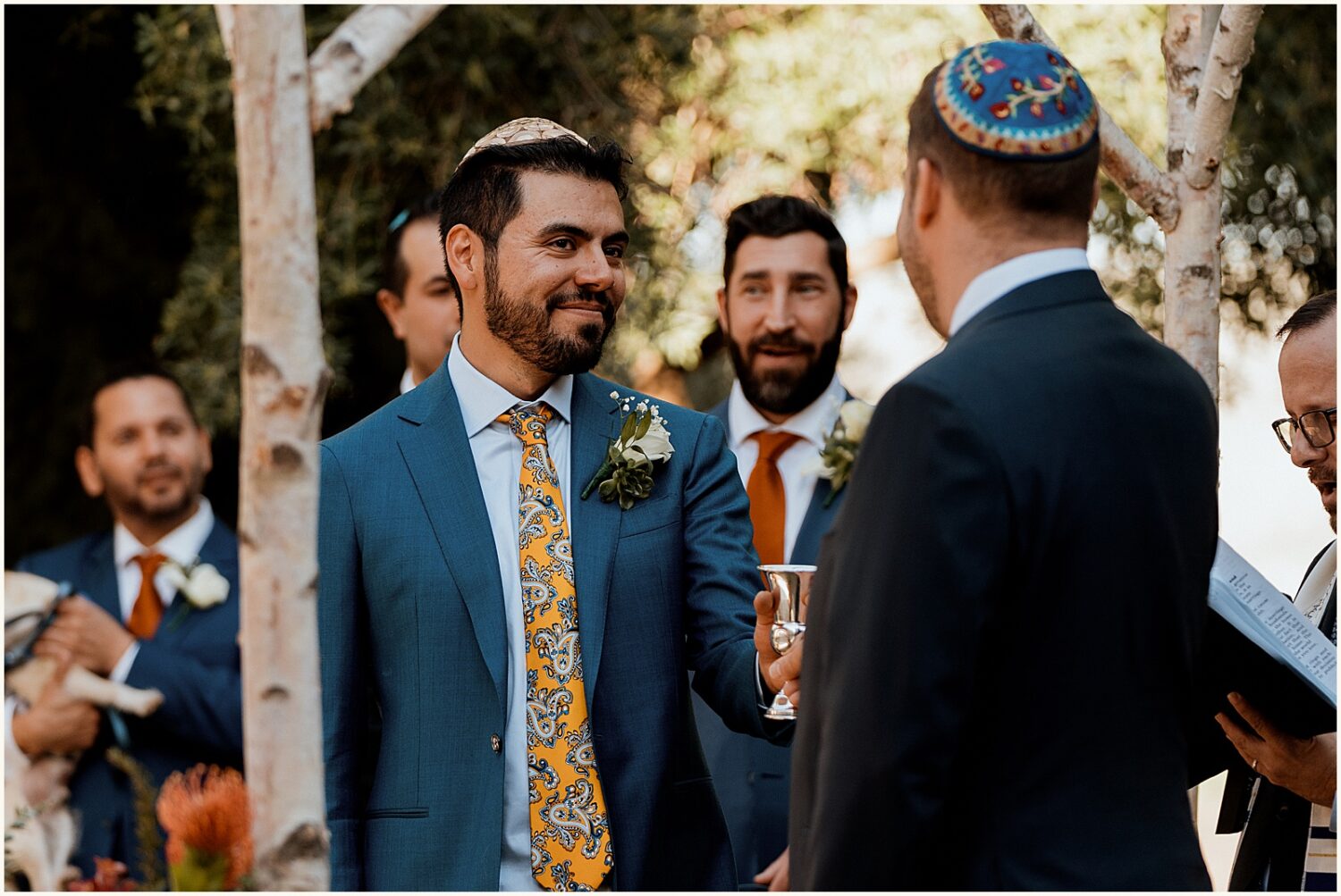 A groom smiles during a ceremony under a chuppah.