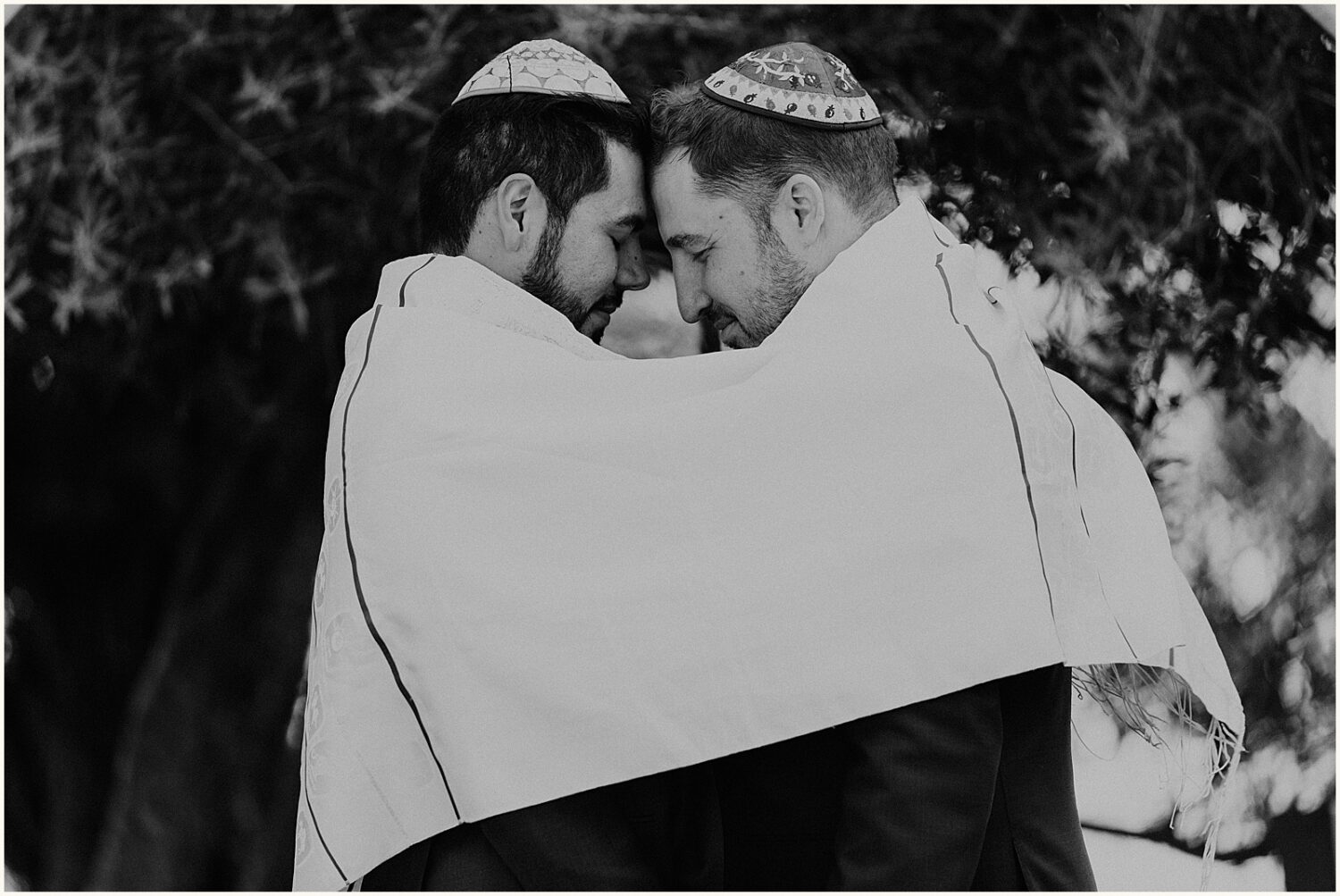 Two grooms touch foreheads while they wear tallit in Jewish wedding photography.