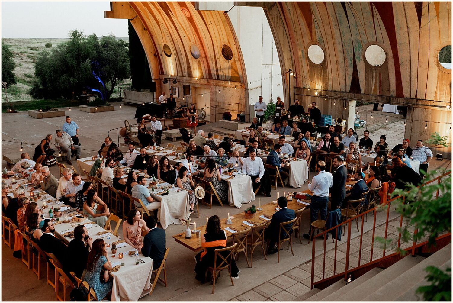 Wedding guests eat dinner at long reception tables at Arcosanti Arizona.