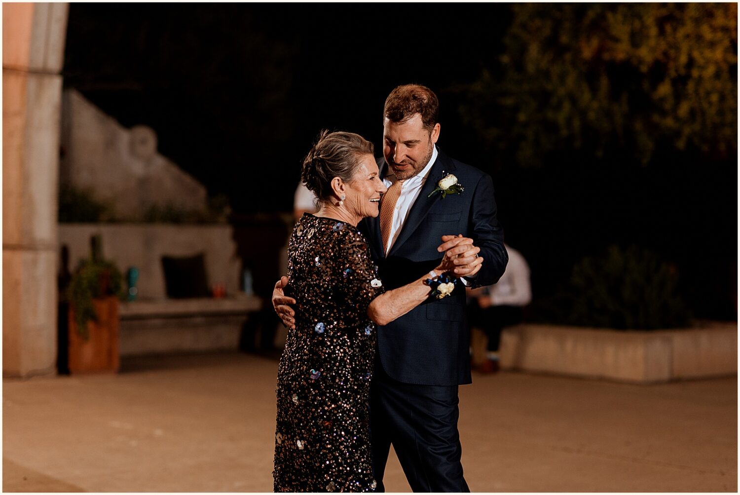 A groom and his mother smile while they dance.