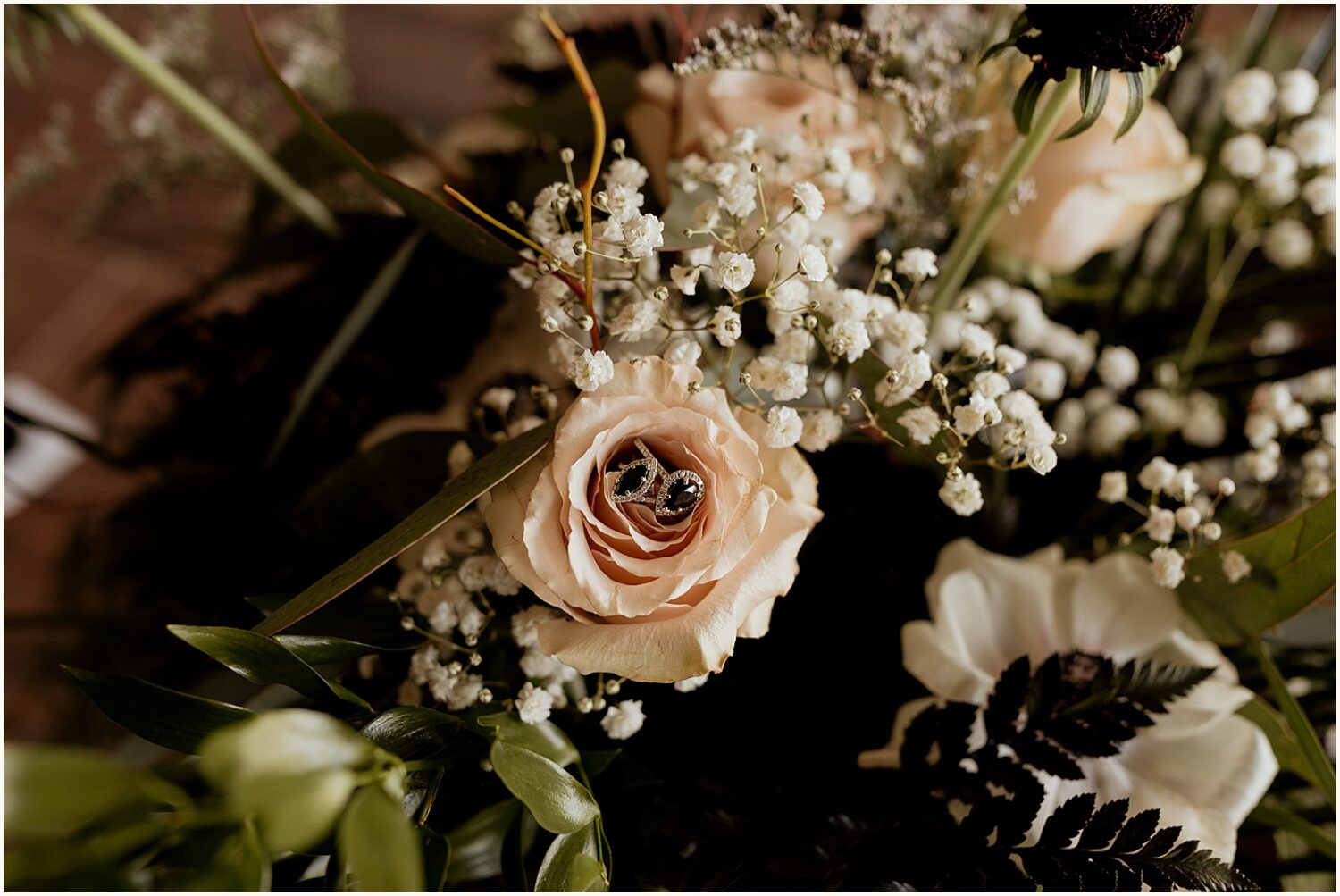 A diamond wedding ring sits on a pale pink rose.