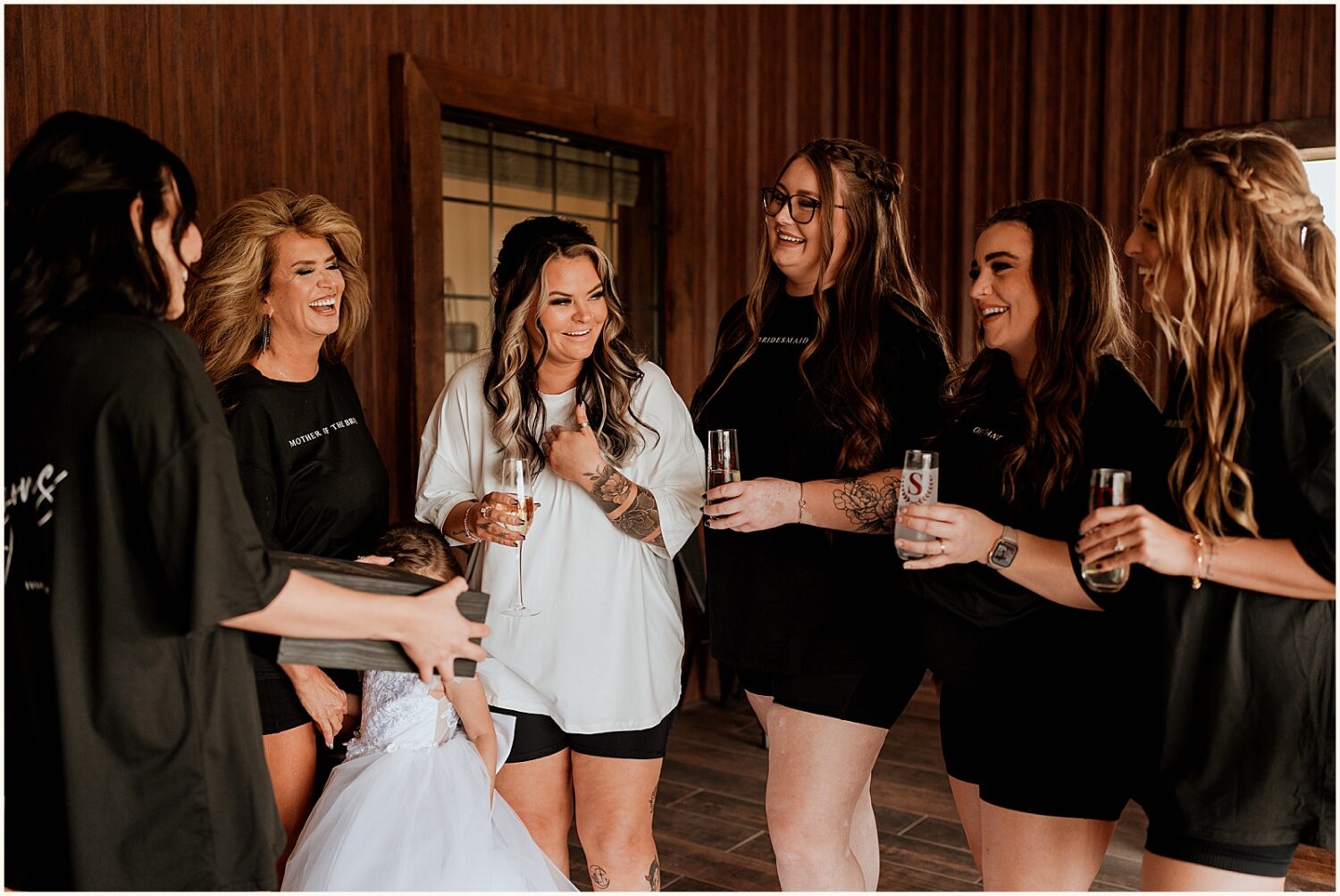 A bride stands surrounded by bridesmaids with champagne flutes.