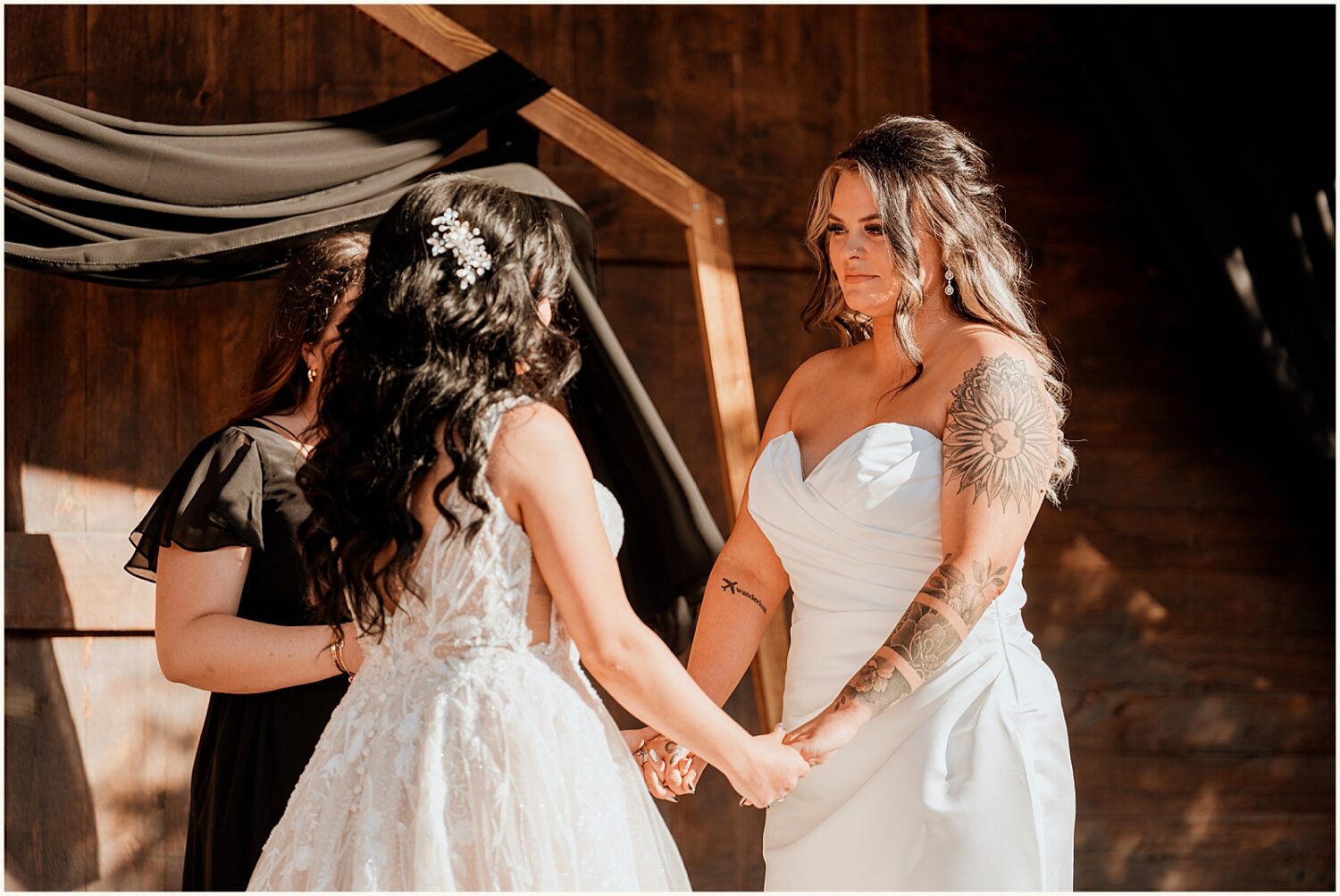 A bride holds her wife's hands and smiles during a ceremony at an Arizona wedding.