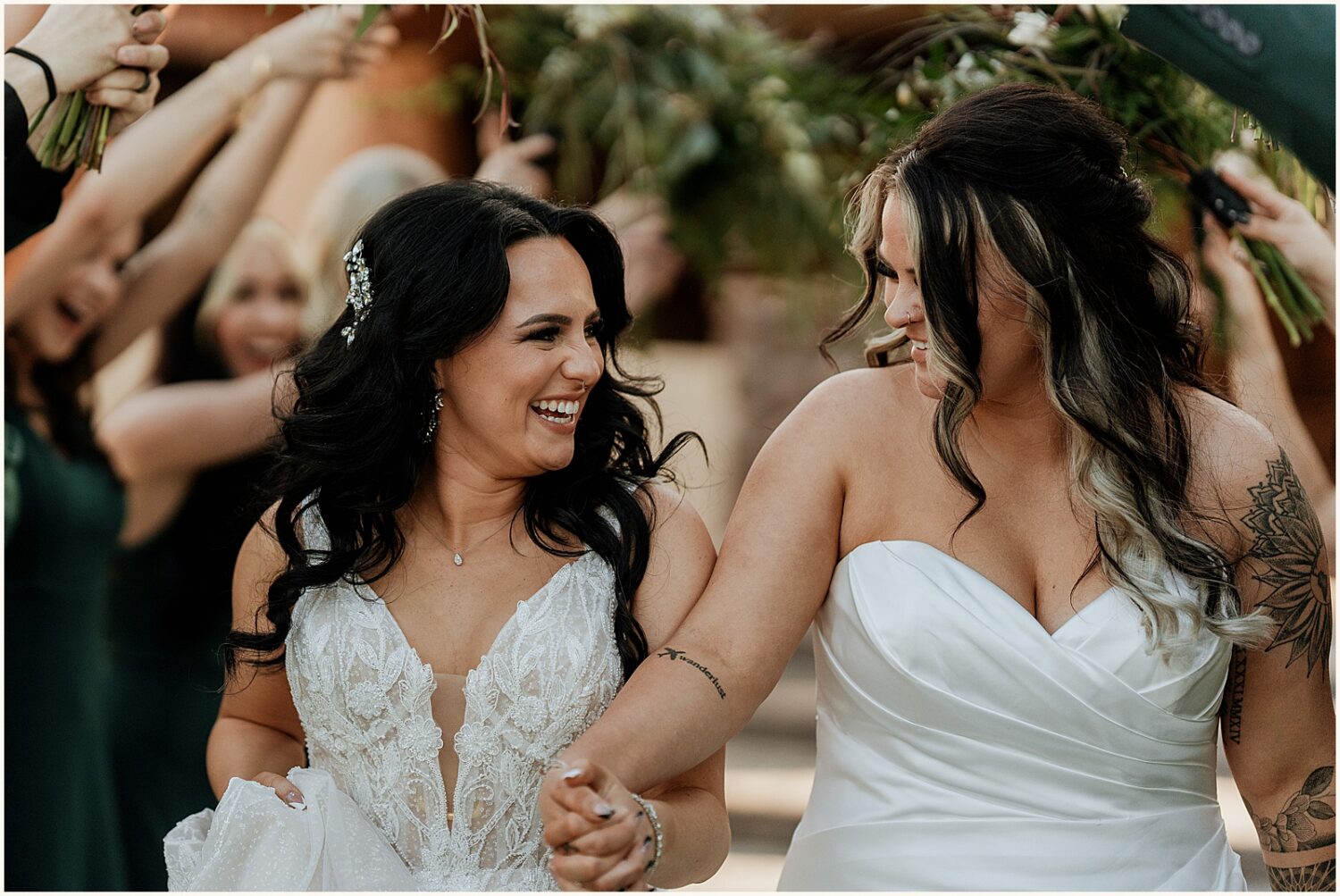 Two brides laugh as they run between lines of bridesmaids.