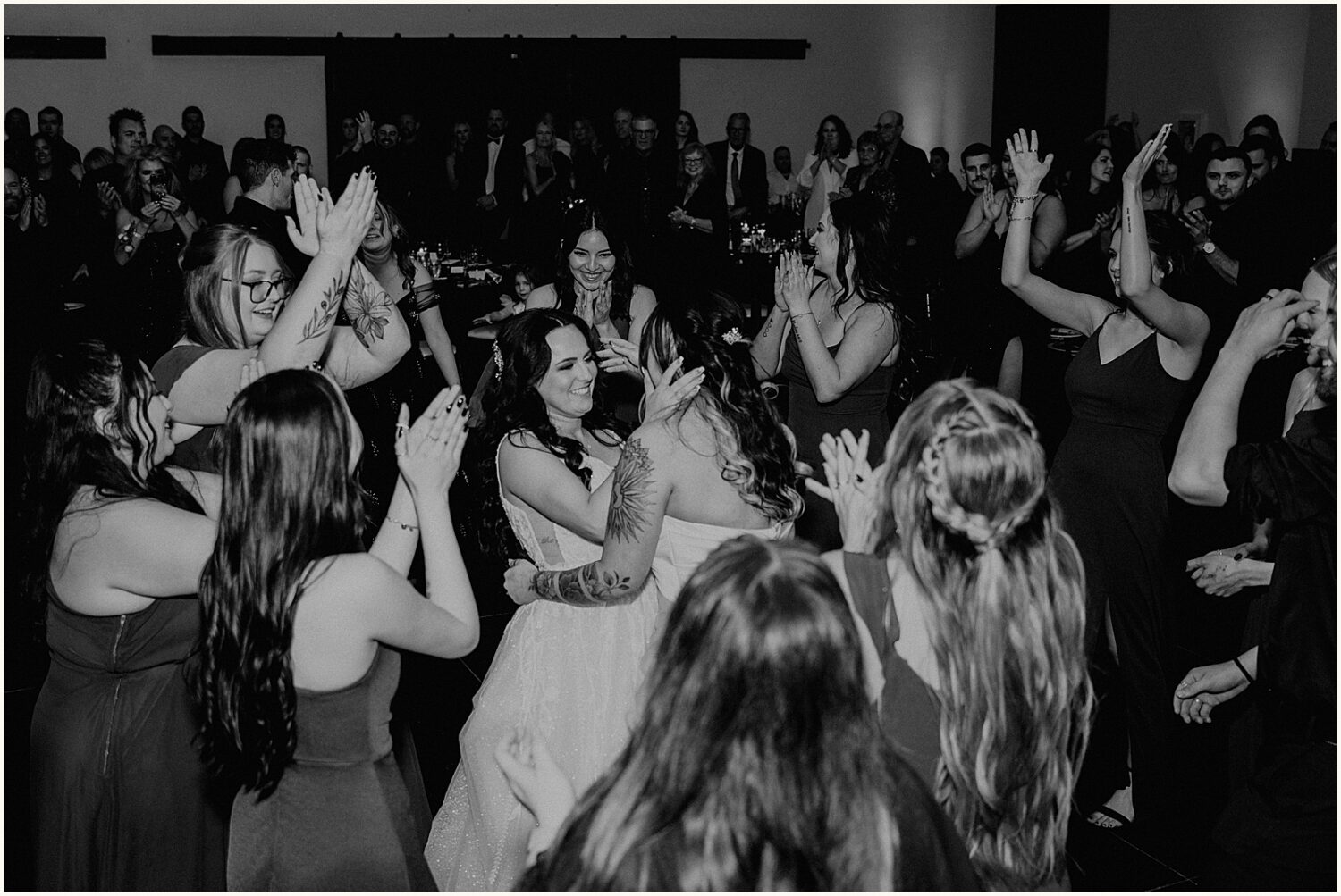 Two brides dance surrounded by friends.